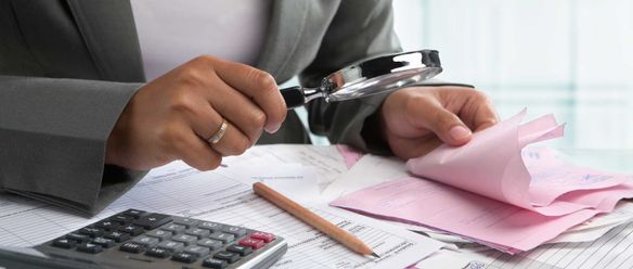 Person examining documents with a magnifying glass at their desk